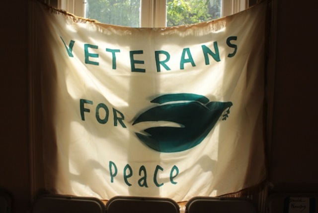 Chapter 25 Veterans for Peace is heir to anti-war history.  Beginning in 1967, this hand-sewn flag made in Madison, Wisconsin, was used by Madison Veterans for Peace in Vietnam at numerous public demonstrations and protests against the war. Chuck Goranson, a Vietnam veteran, was a grassroots organizer of the group. “Vietnam” was dropped from the group’s name in 1970, when the war was expanded into Cambodia and Laos. Clarence Kailin Chapter 25 Veterans for Peace is a 21st century renewal of the earlier veterans for peace organization. This photo, by Chapter 25 member Phillip Fransen, was taken during the peace rally May 25, 2015, at the Gates of Heaven in James Madison Park. The aging flag serves as a reminder that veterans have long been active in the peace movement.  (Photo by Phillip Fransen)